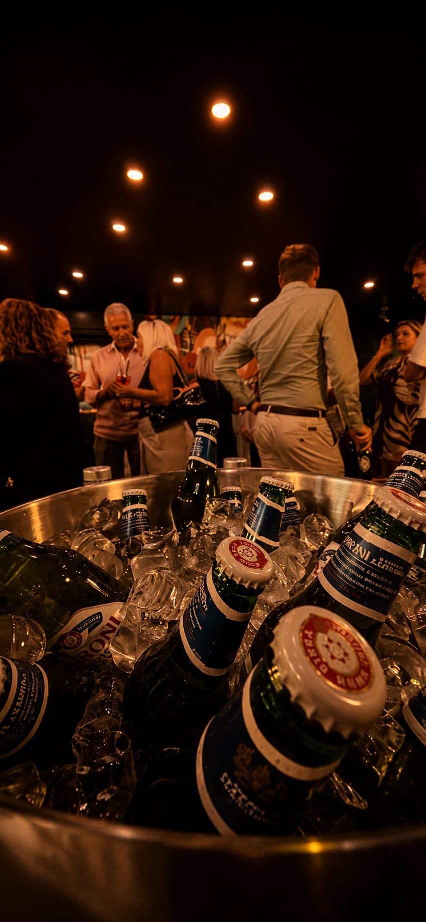 A steel bucket of beer bottles on ice in the foreground, with guests chatting in the softly lit NORA dining room behind