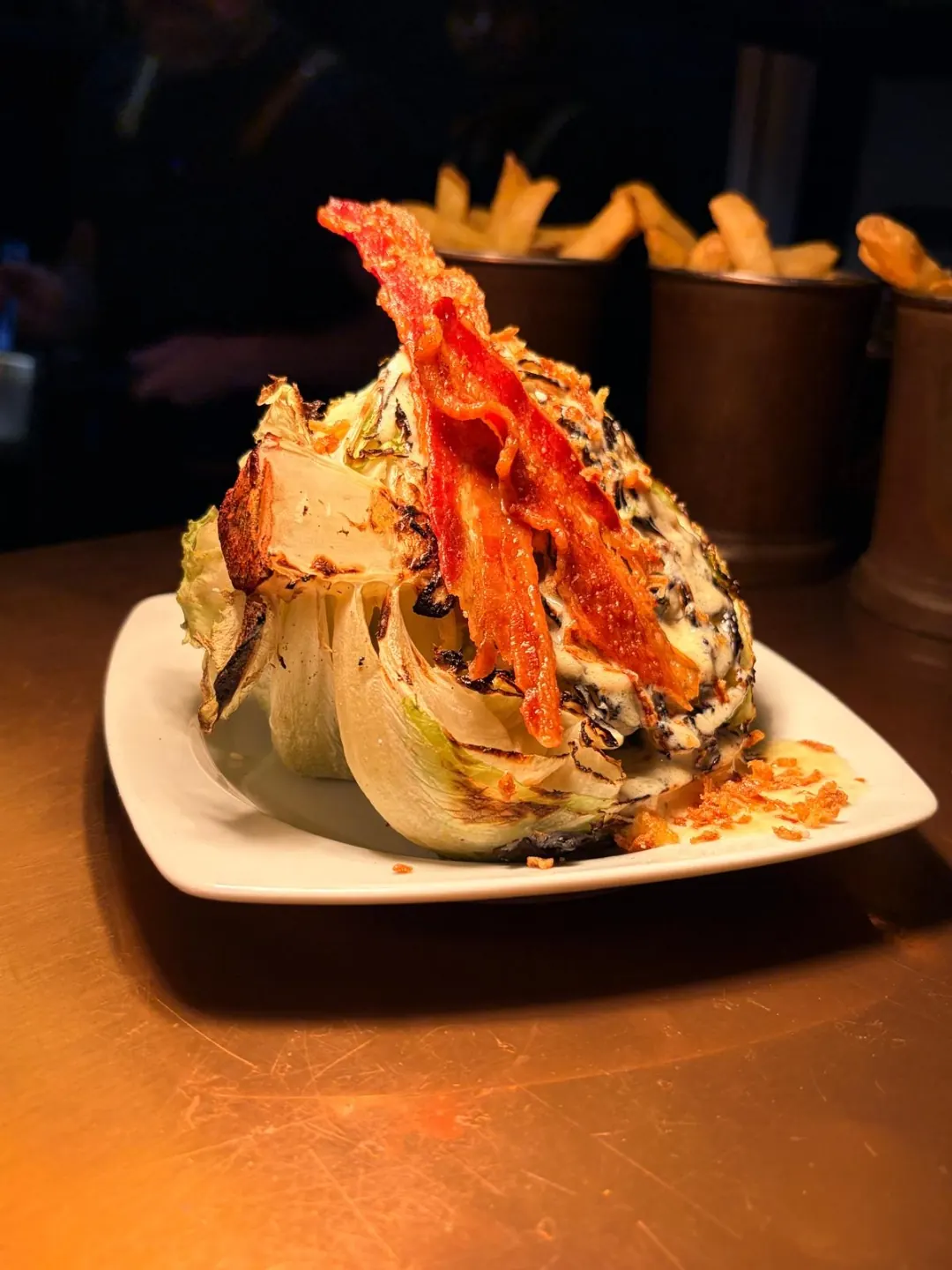 Charred iceberg lettuce wedge with a creamy dressing and crispy bacon on a white plate