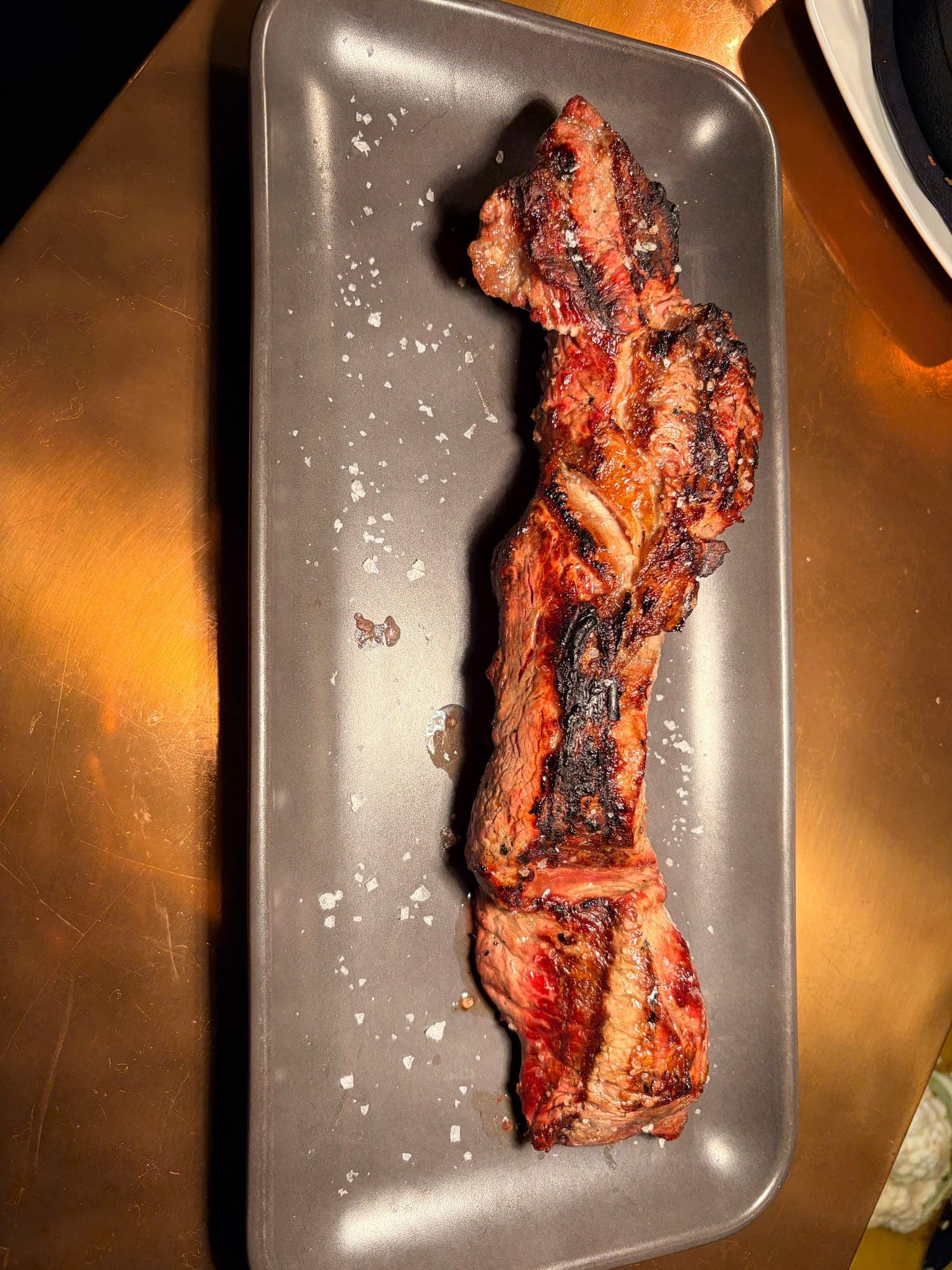 Charred grilled steak on a grey plate, finished with flaky salt