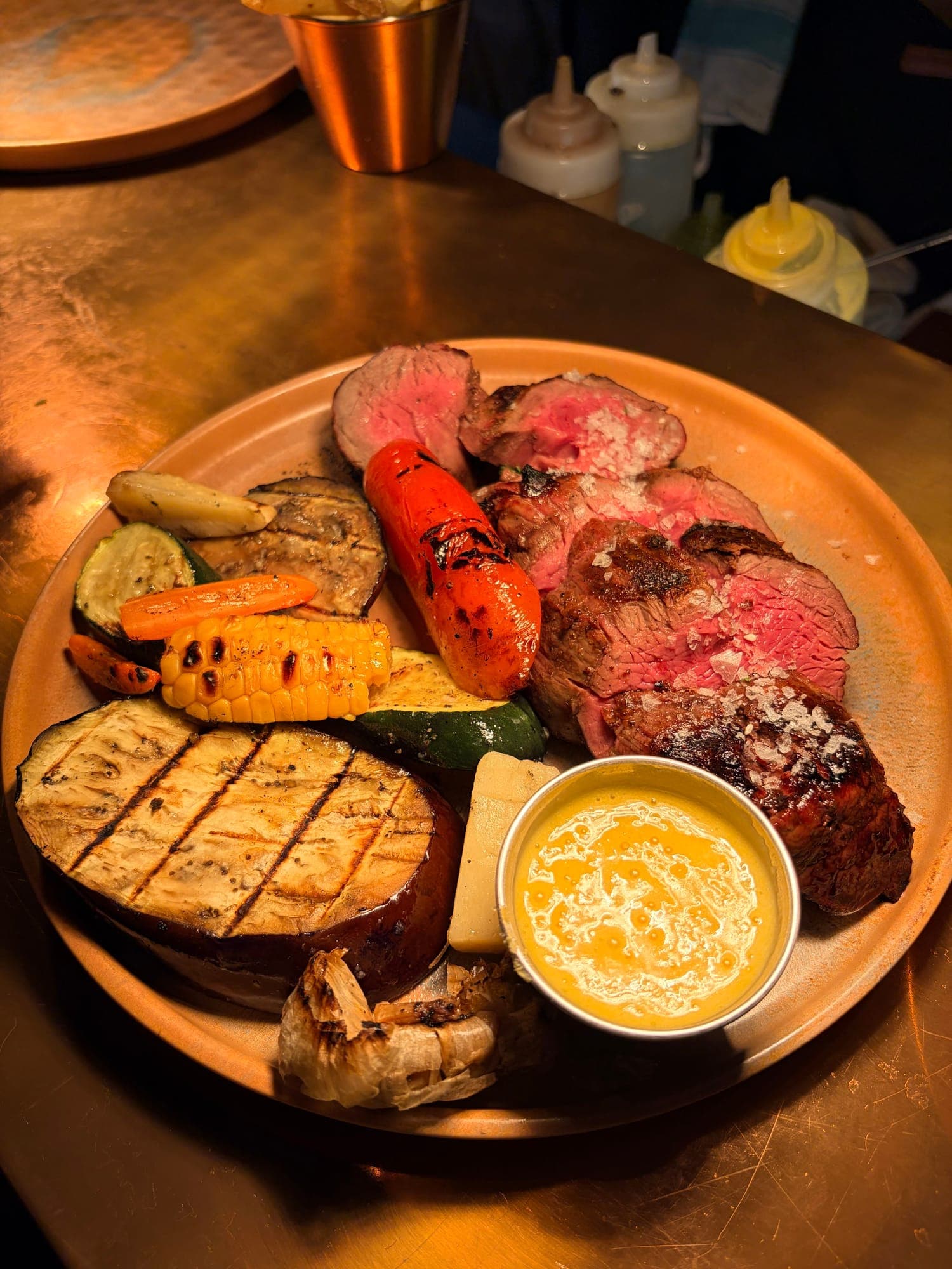 Sliced fire-grilled steak with charred vegetables and sauce on a terracotta plate