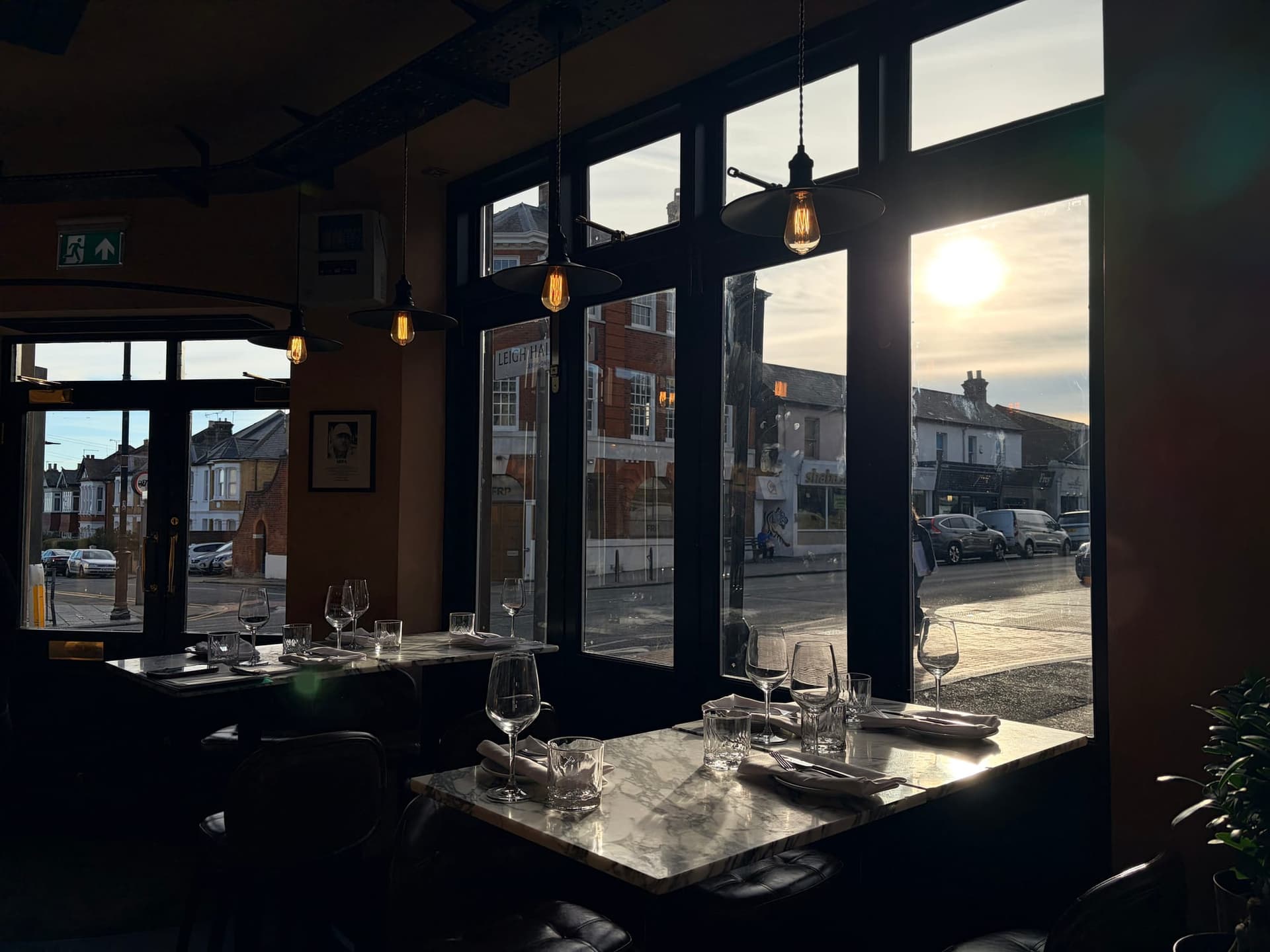 Marble-topped tables laid with wine glasses beside tall windows, with evening sun over the street outside
